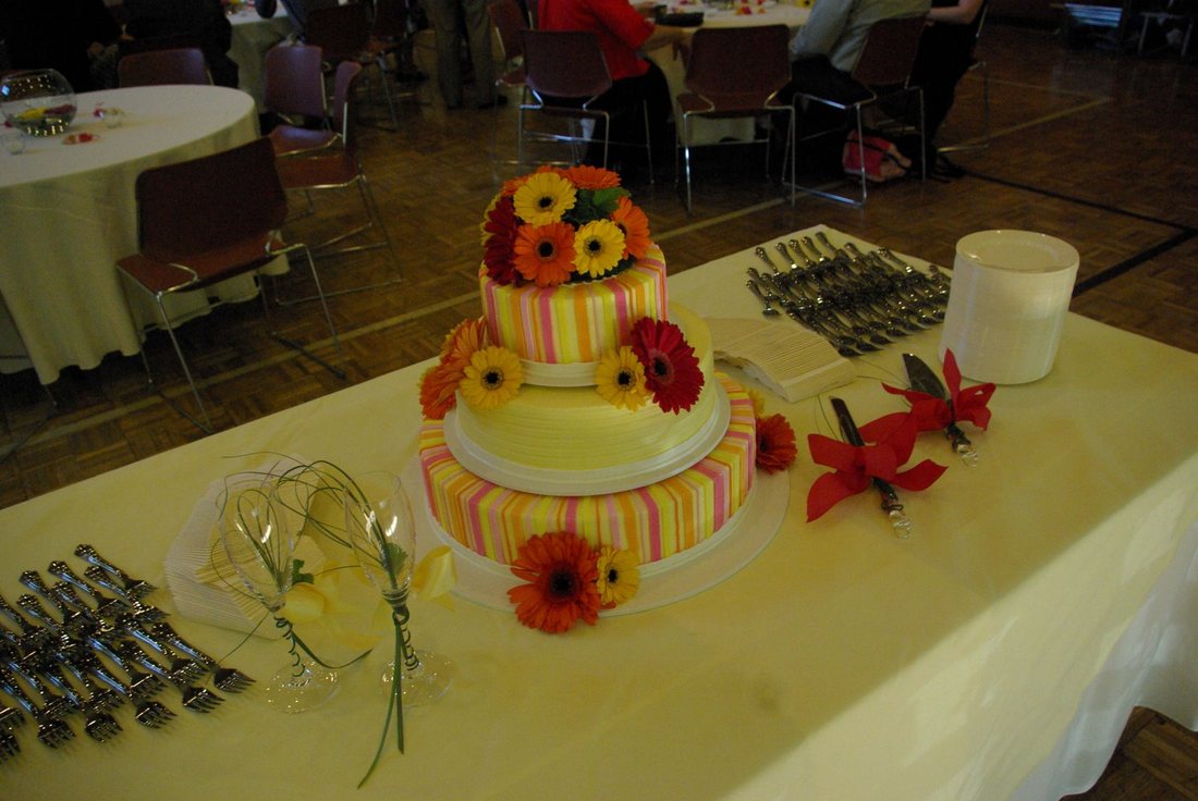 Three-tier striped wedding cake decorated with orange and yellow gerbera daisies