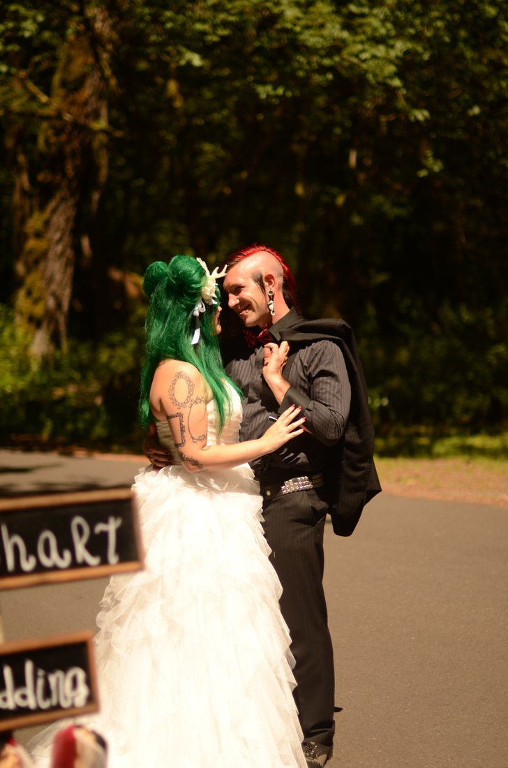 Bride with green hair and a white floral crown facing her groom on a forest path at Oxbow Park
