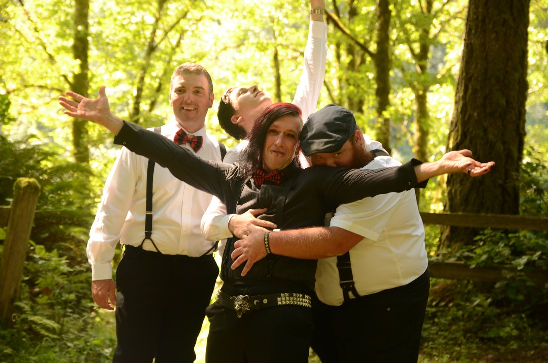 Three groomsmen in bow ties and suspenders clowning for the camera in the trees