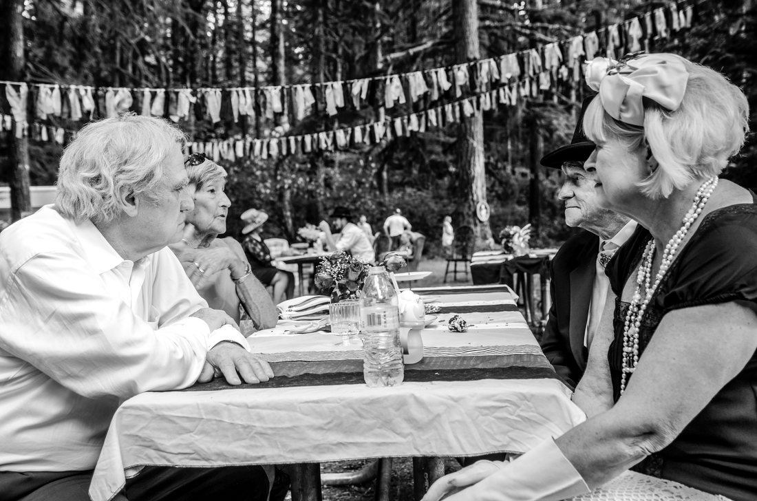 Black and white photograph of older guests talking across a table under bunting
